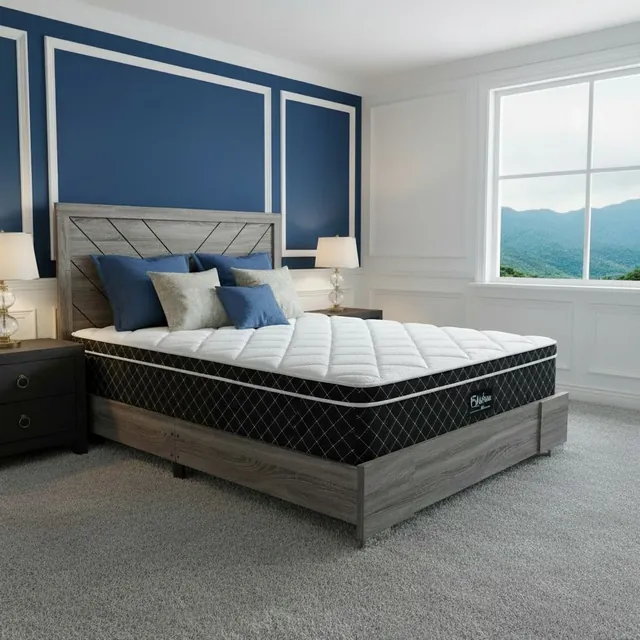 White quilted mattress with black diamond-quilted sides on a gray wood bed with blue and sage pillows, mountain view through the window
